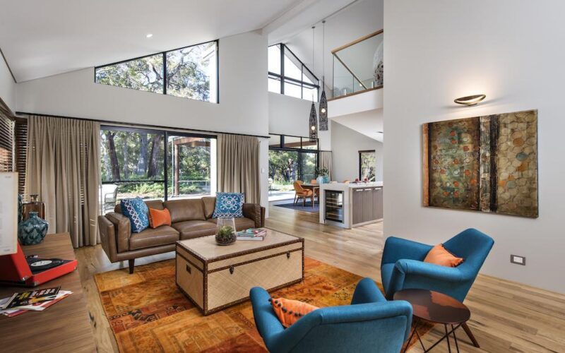 bright open plan living room with raked ceilings, big windows and coloured accessories
