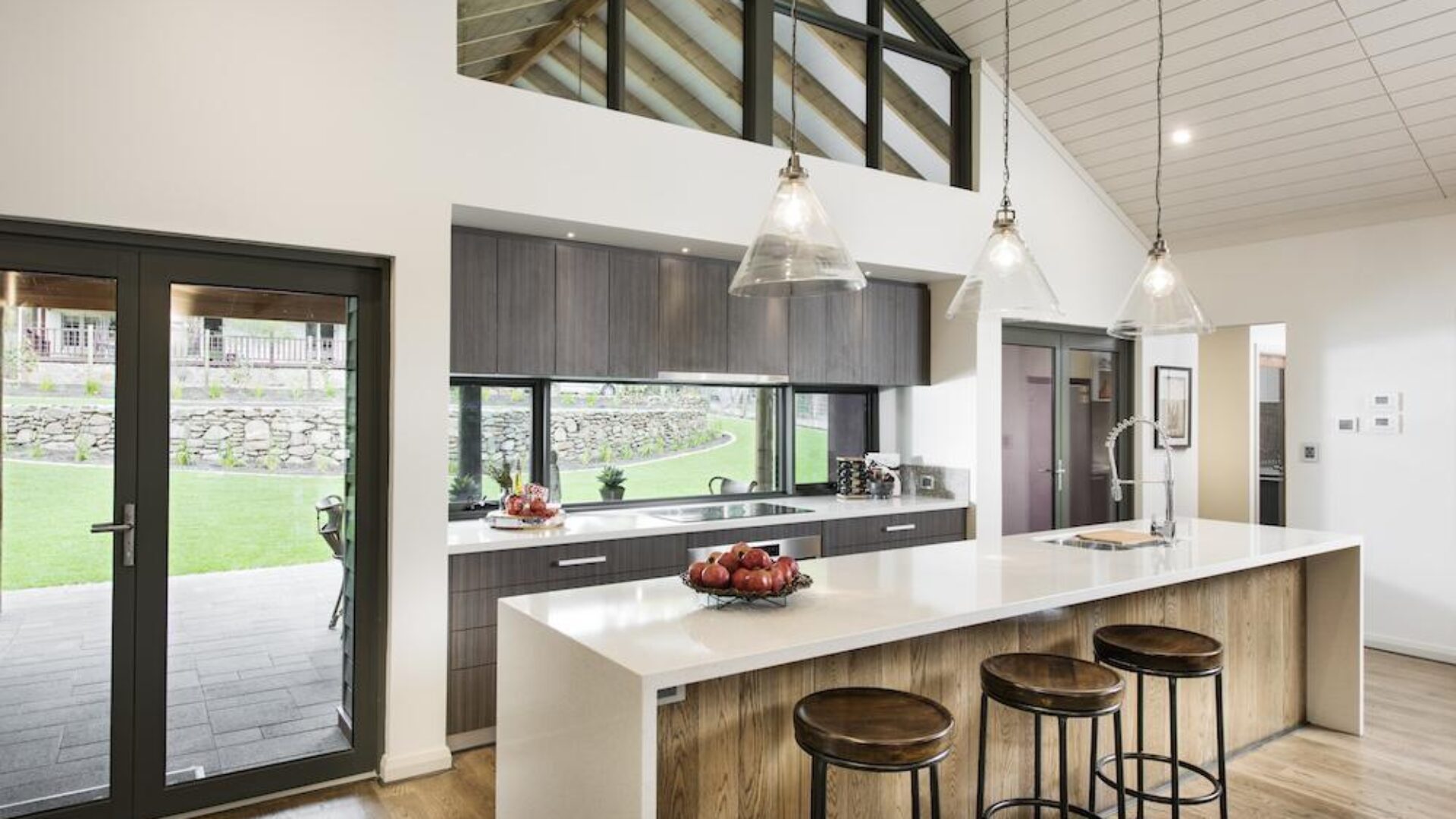 Kitchen with white stone island bench, glass pendant lights and rural outlook