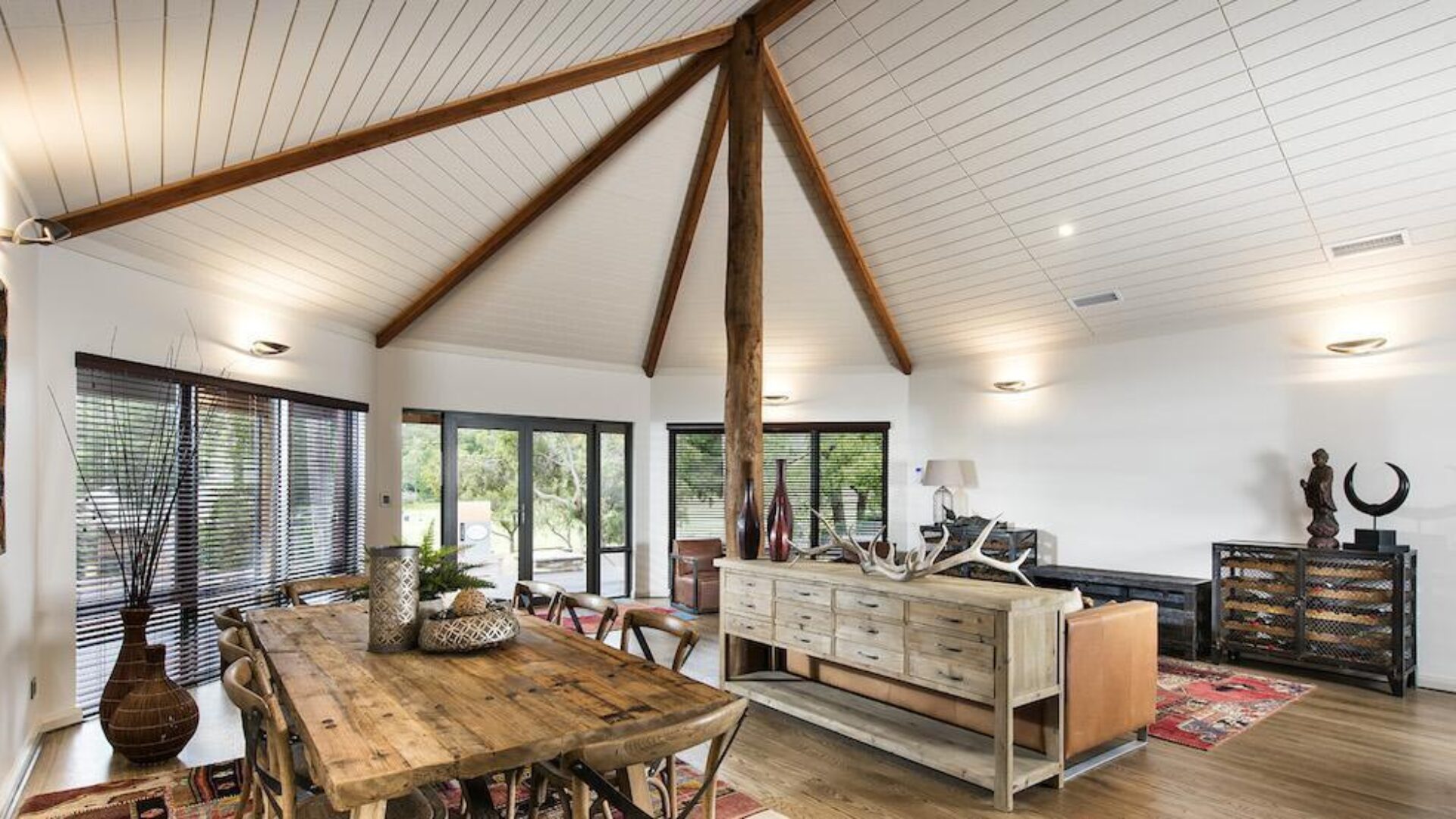 Living area with raked ceiling, exposed timber truss and rustic dining table