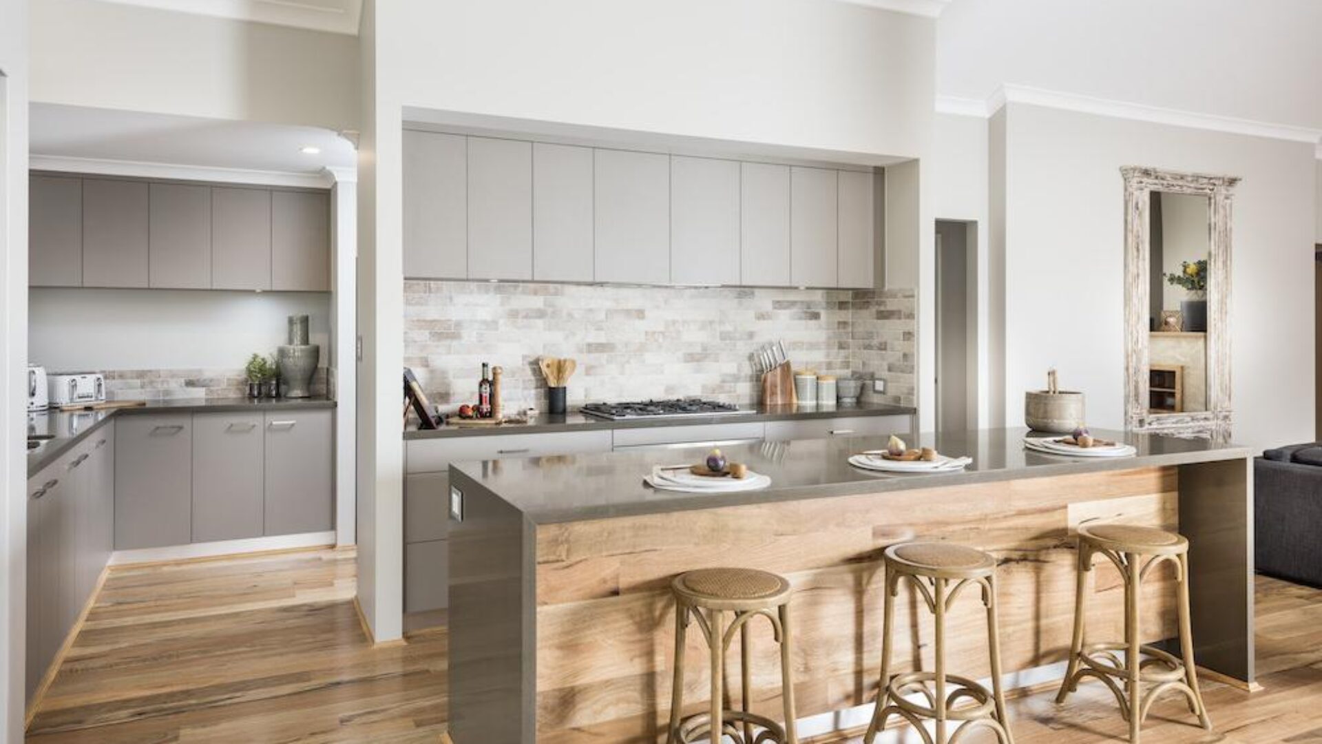 Kitchen with timber island bench, rattan bar stools and brick splashback