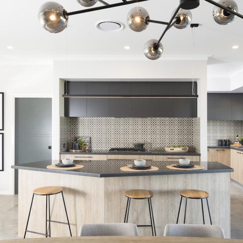 Kitchen with grey stone island bench, herringbone splashback and timber stools