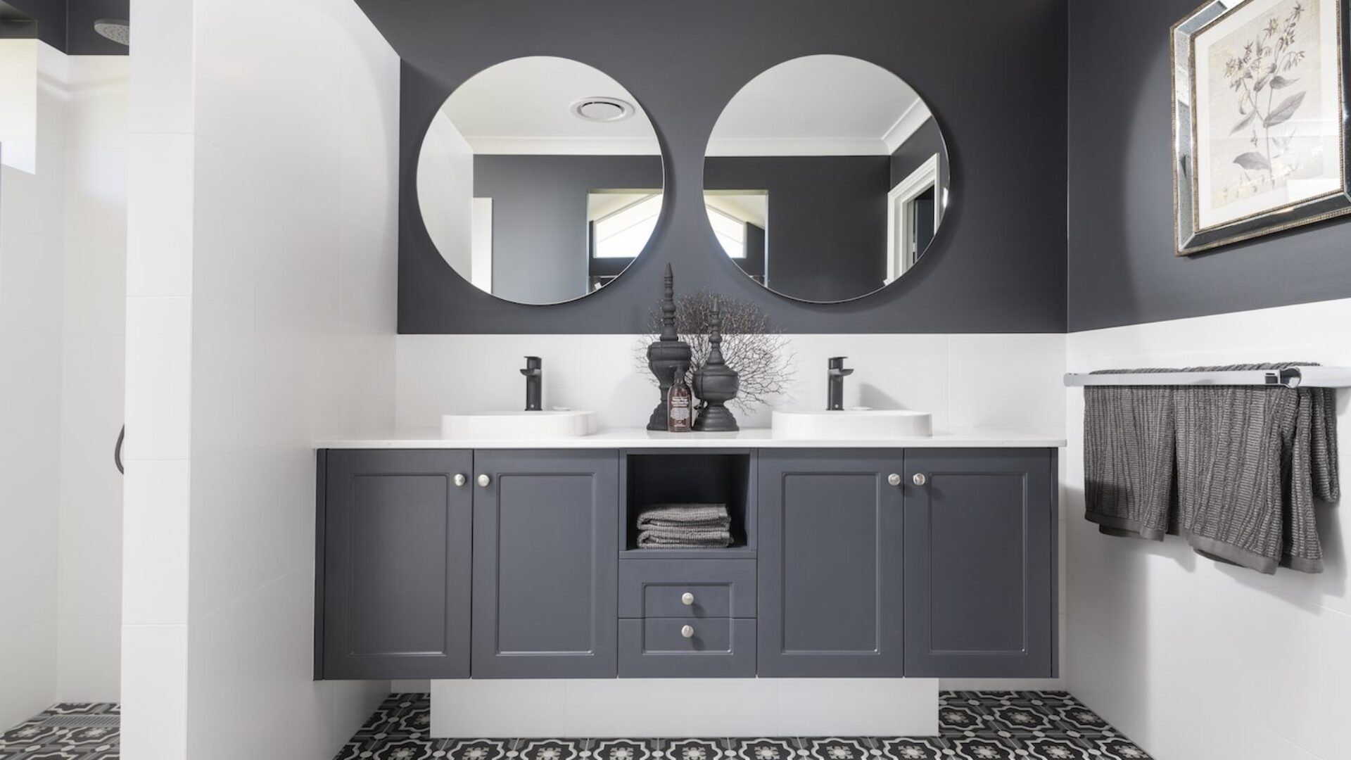 Bathroom with charcoal cabinetry, twin round mirrors and patterned floor tiles