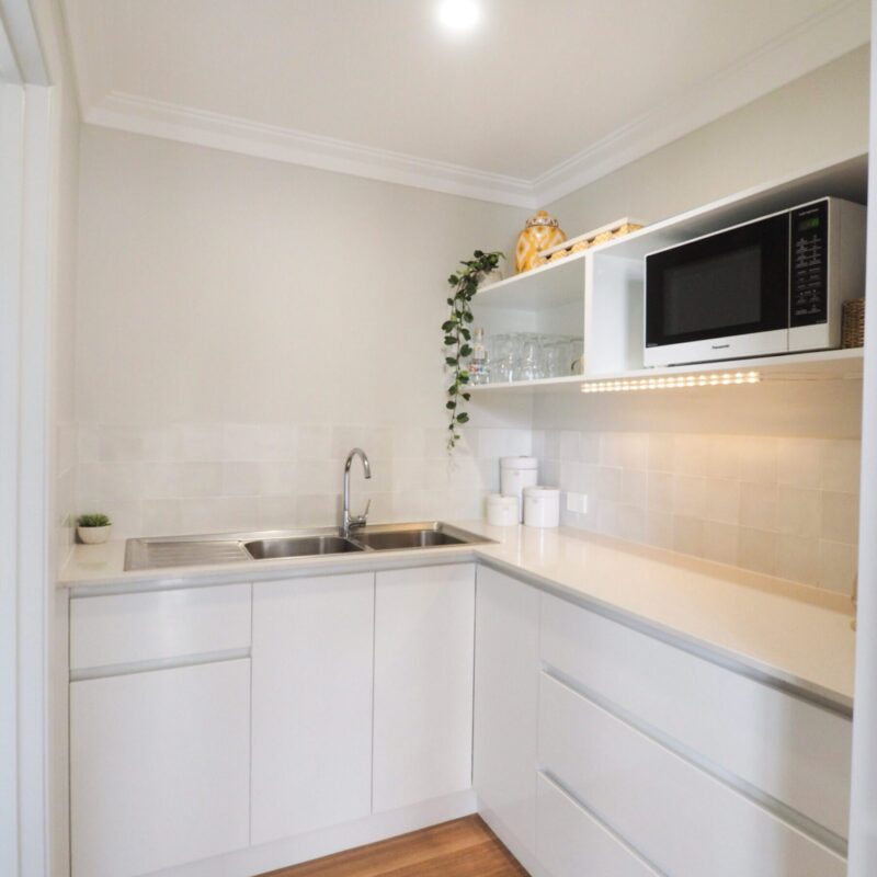 Compact scullery with white cabinetry, sink and microwave