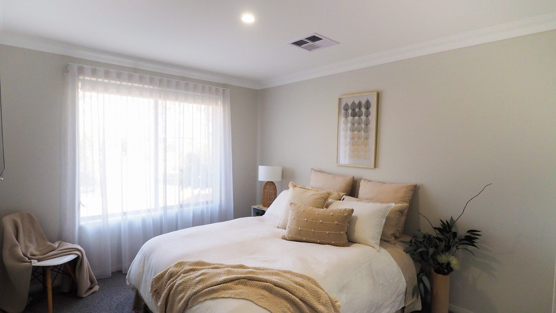 Bedroom with sheer curtains, neutral bedding and framed artwork