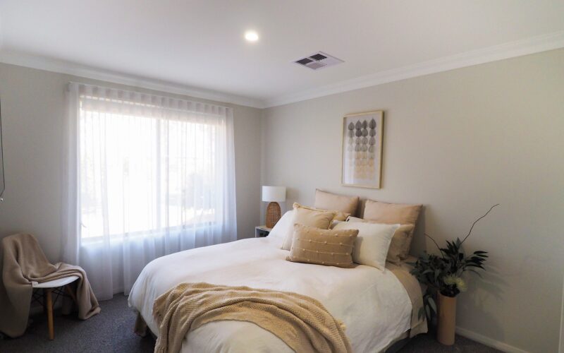 Bedroom with sheer curtains, neutral bedding and framed artwork