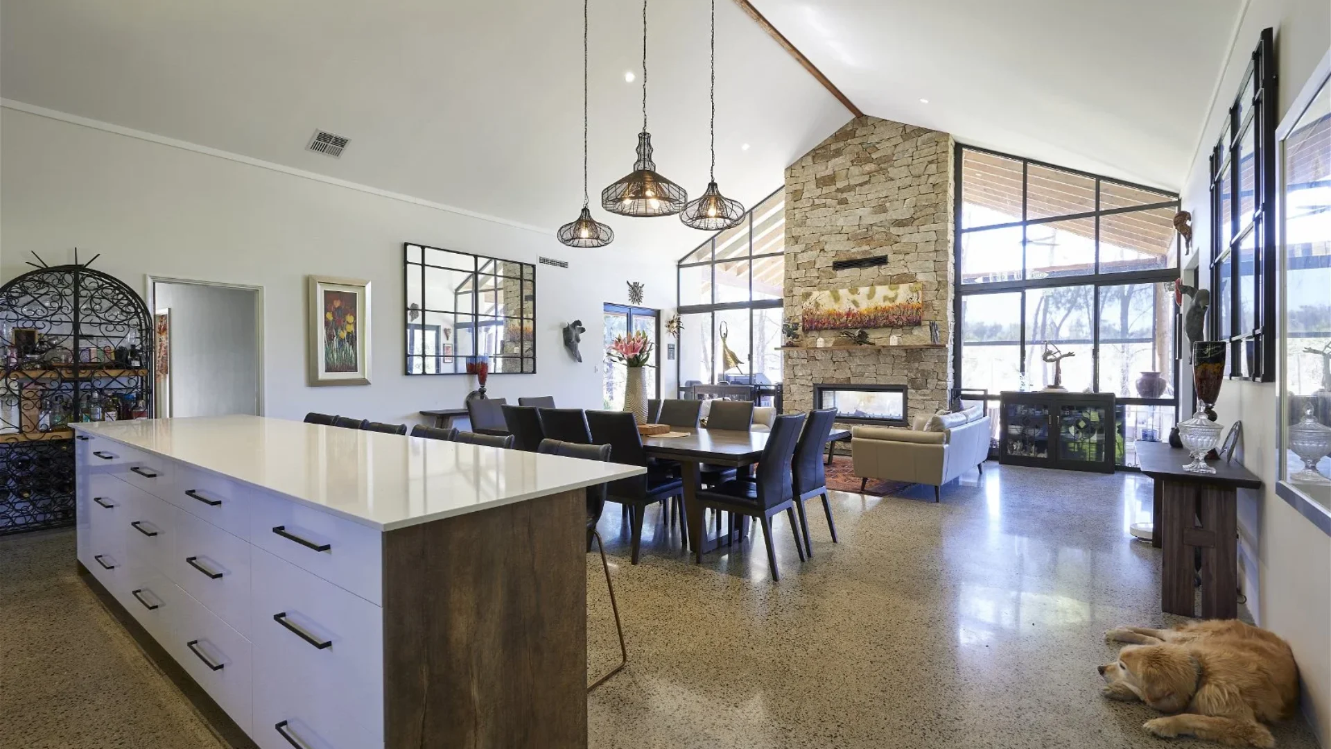 Open plan kitchen and living with stone fireplace, polished concrete floor and dog