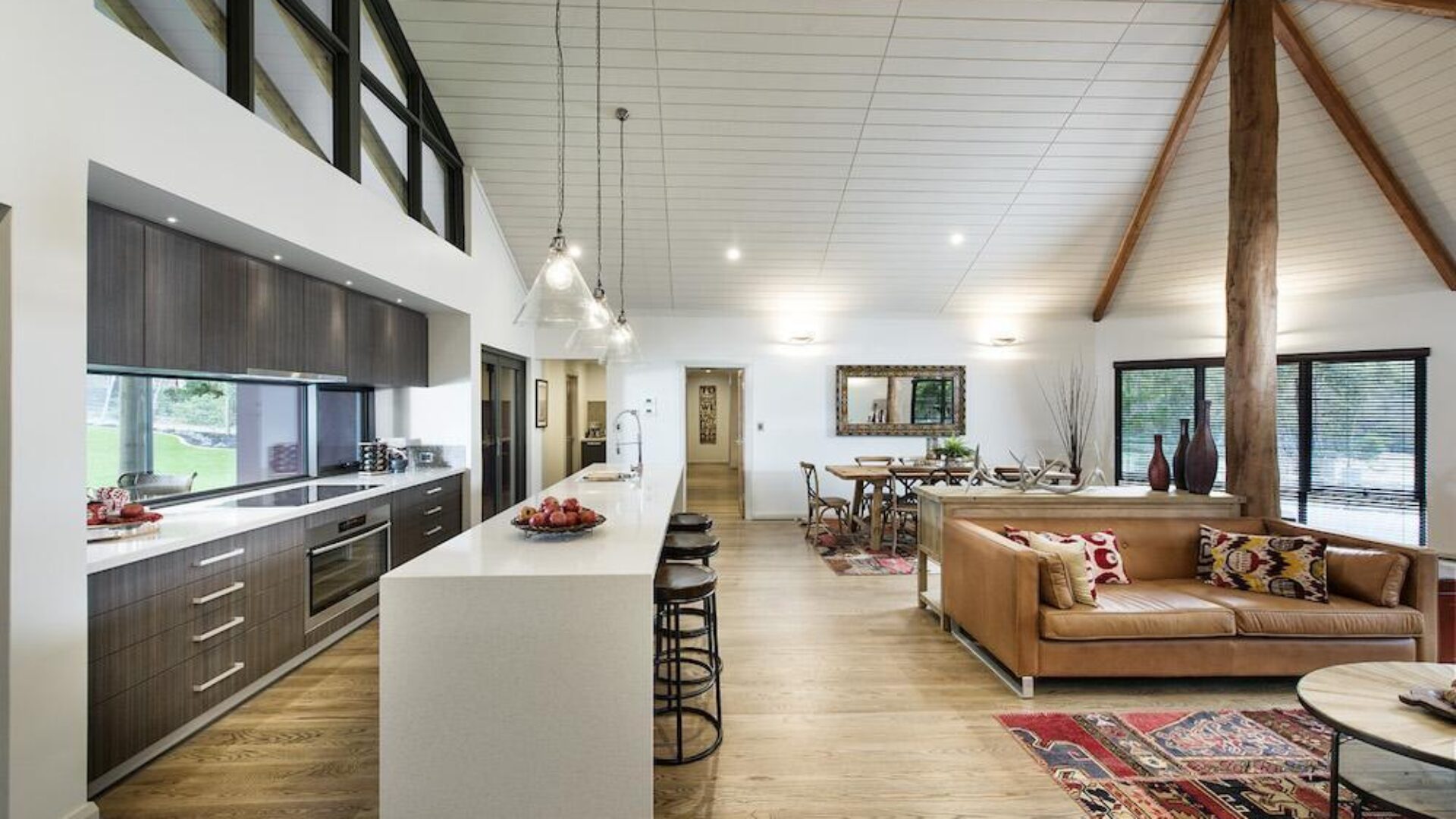 Open plan kitchen and living with exposed timber truss and leather sofa