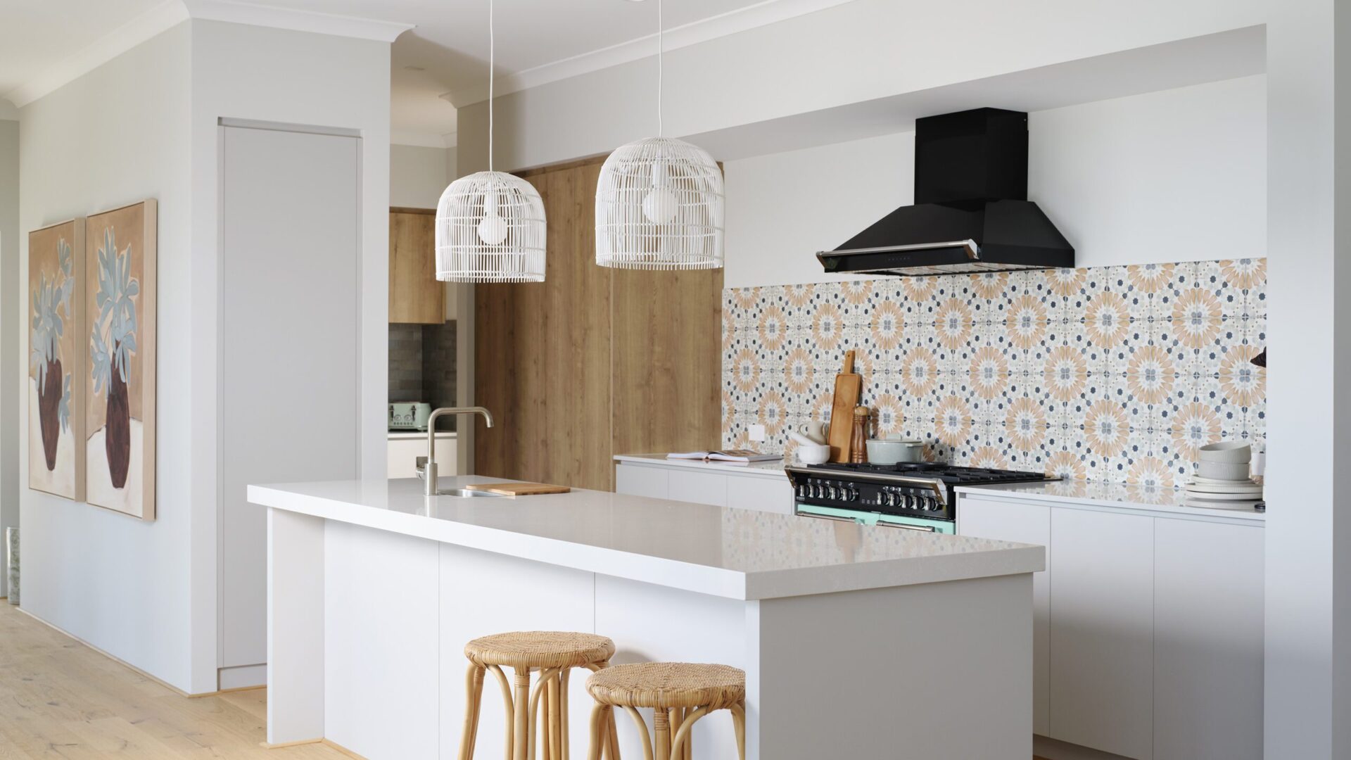 Kitchen with patterned tile splashback, white island bench and rattan stools