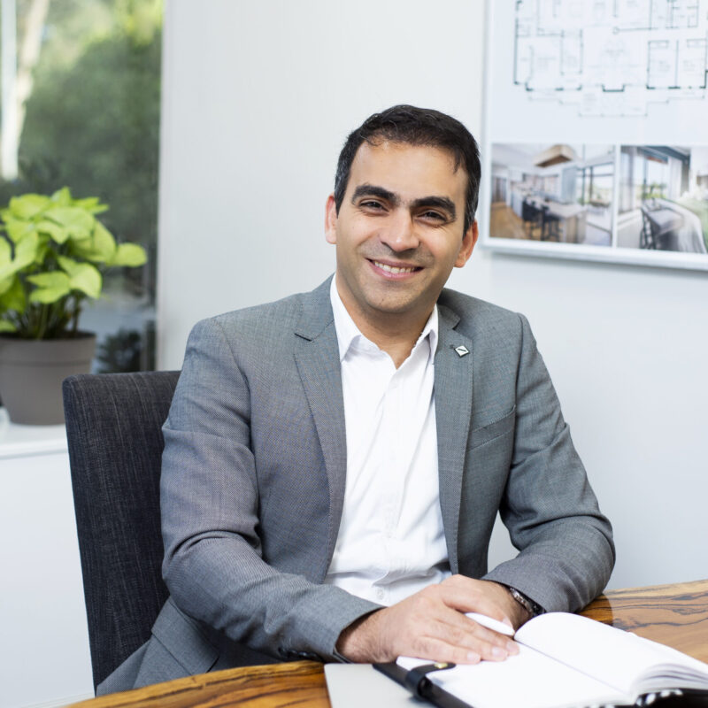 Portrait of Ehsan at a desk with floor plans behind