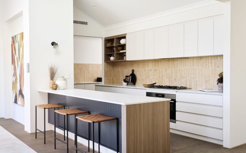 Kitchen with white island bench, timber splashback and black bar stools