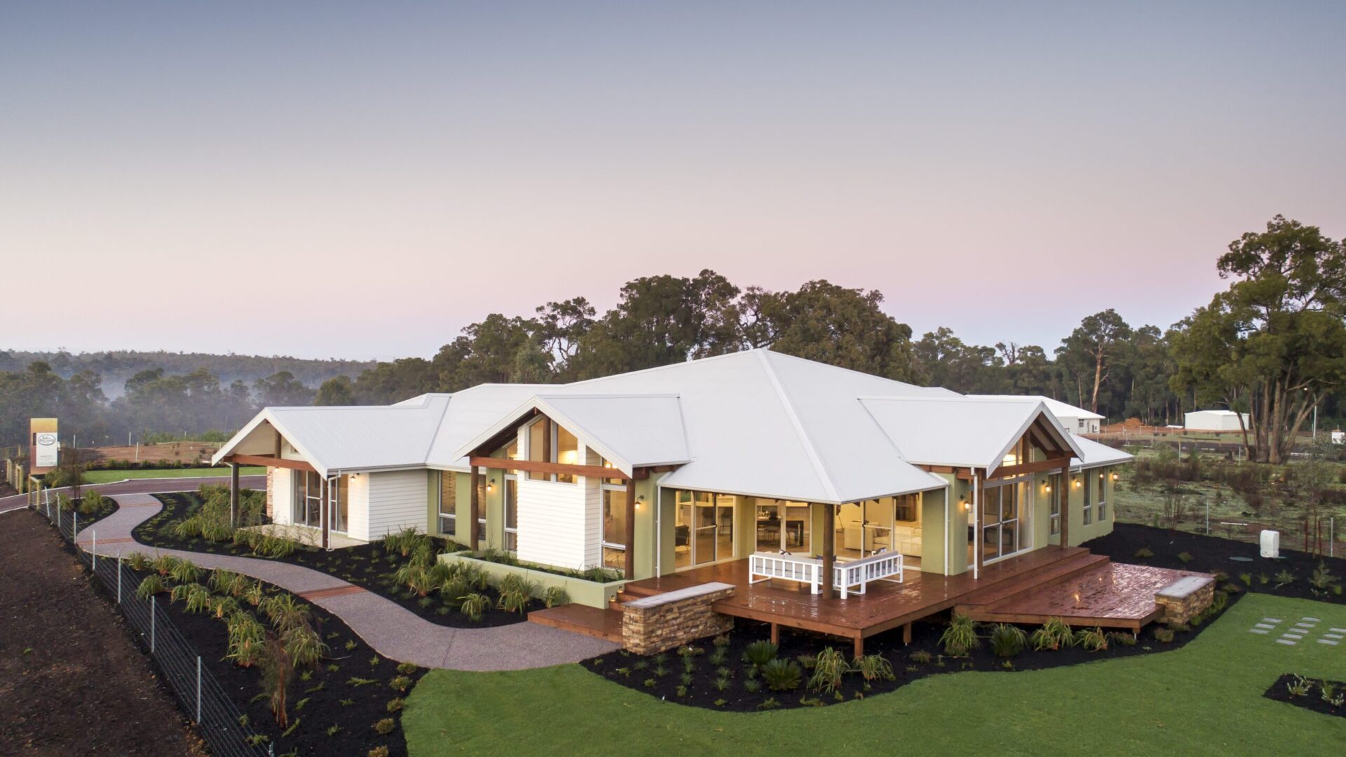Homestead with wraparound verandah beside a landscaped dam and timber deck