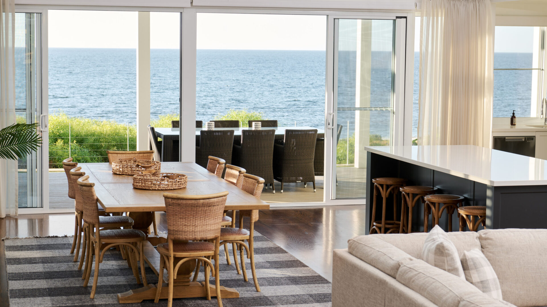 Dining and kitchen with rattan chairs and ocean views through bifold doors