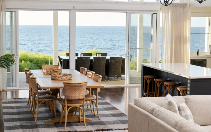 Dining and kitchen with rattan chairs and ocean views through bifold doors