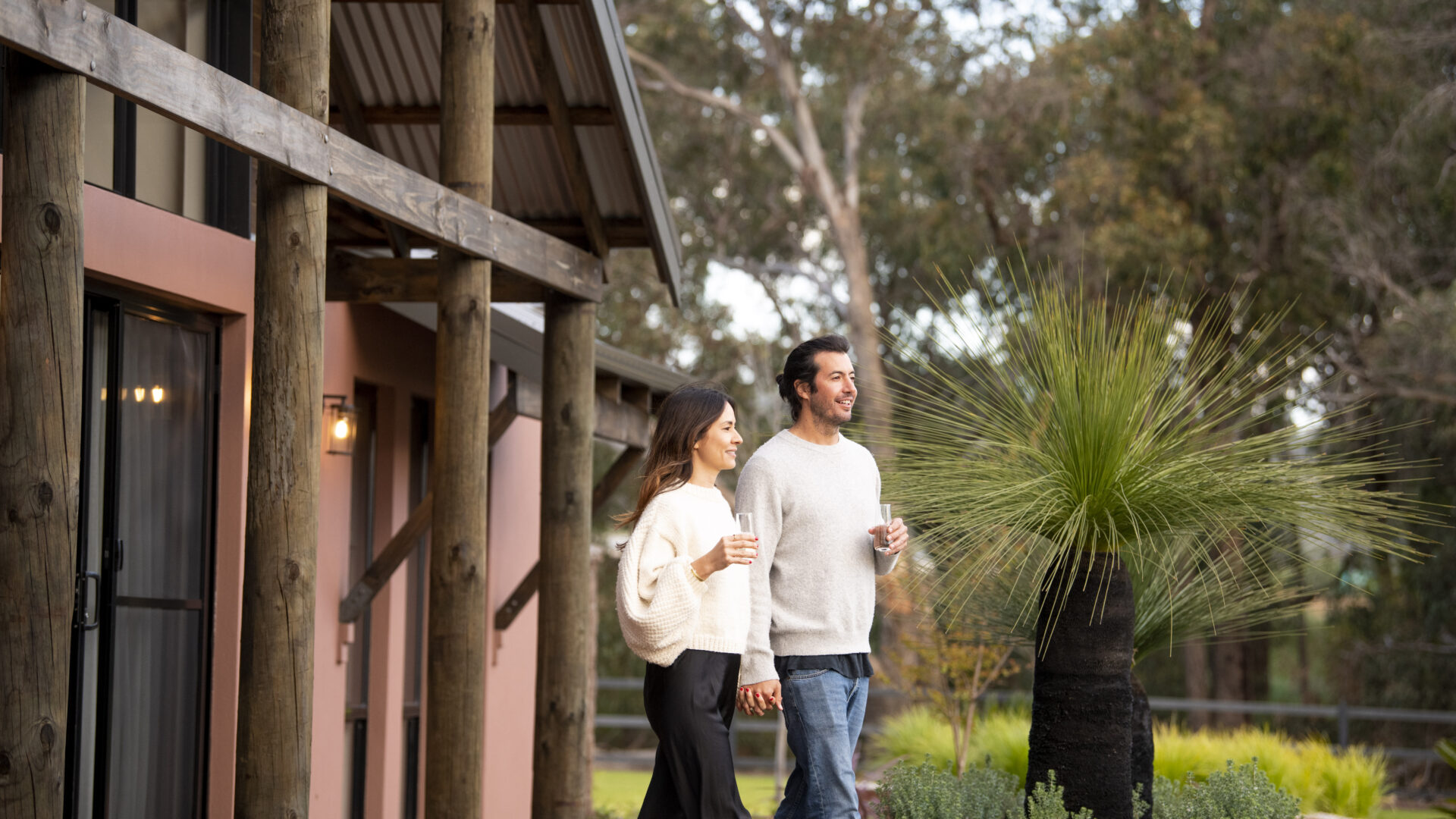 Couple walking outside a rural residential property with timber posts and native landscaping by Rural Building Co.