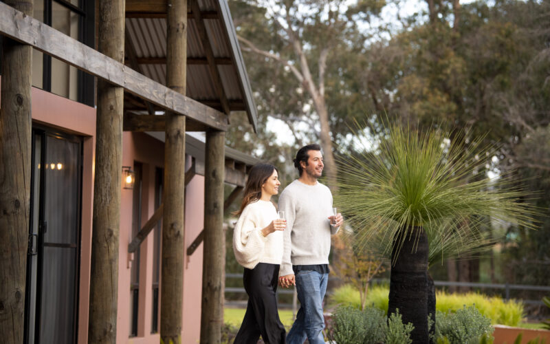 Couple walking outside a rural residential property with timber posts and native landscaping by Rural Building Co.