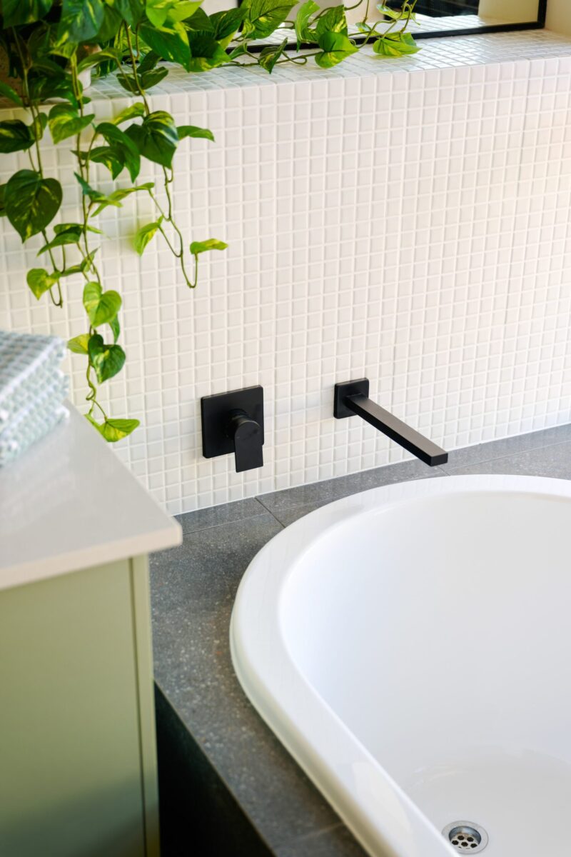 Bath detail with mosaic tiling, black tapware and trailing plant
