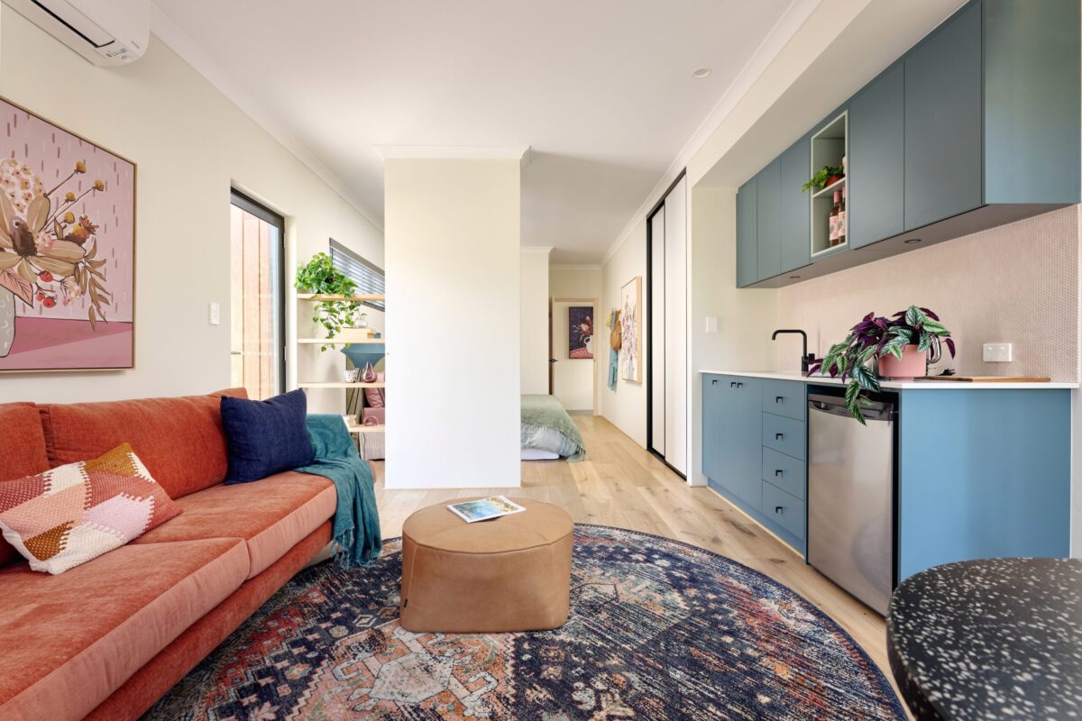 Living area with coral sofa, patterned rug and blue kitchen joinery beyond