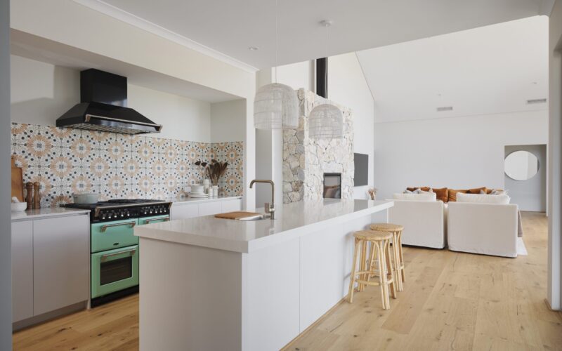 Kitchen with patterned tile splashback, white island bench and green freestanding cooker