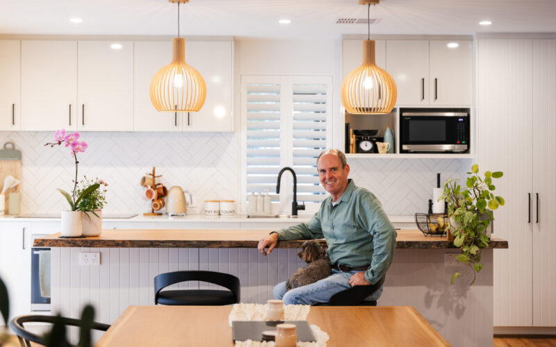 Client seated at the kitchen island bench of his completed home with his dog